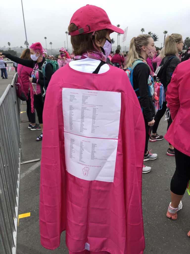 Cathy M. wears a pink cape that has names of people impacted by breast cancer.